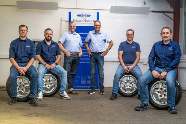 Team von Kfz-Sachverständigen in Werkstatt, sitzt auf Autoreifen, Porträt