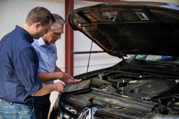 Zwei Kfz-Mechaniker prüfen Motorraum mit Tablet in der Autowerkstatt
