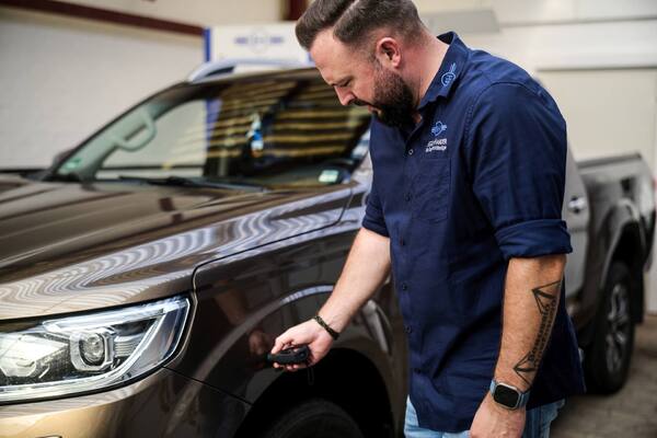 Kfz-Meister prüft Lackschaden am Auto in Werkstatt mit Messgerät