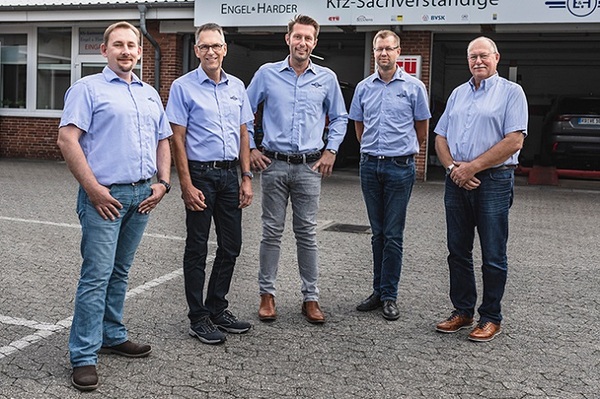 Fünf Kfz-Sachverständige stehen vor einem Gutachterbüro und lächeln in die Kamera.