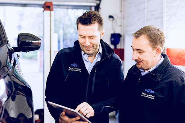 Zwei Kfz-Experten in einer Autowerkstatt prüfen Reparaturdaten auf einem Tablet.