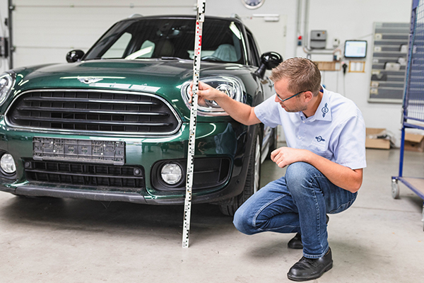 KFZ-Gutachter misst Fahrzeughöhe an grünem Auto in Werkstatt zur Schadensbewertung.